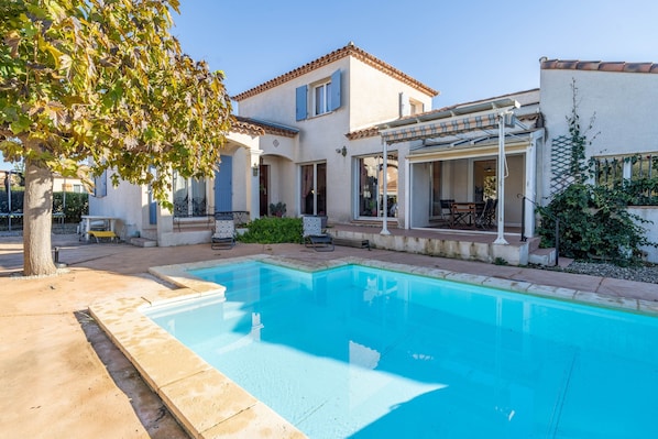 A house with a swimming pool, a patio with outdoor furniture, and a covered area with a pergola.