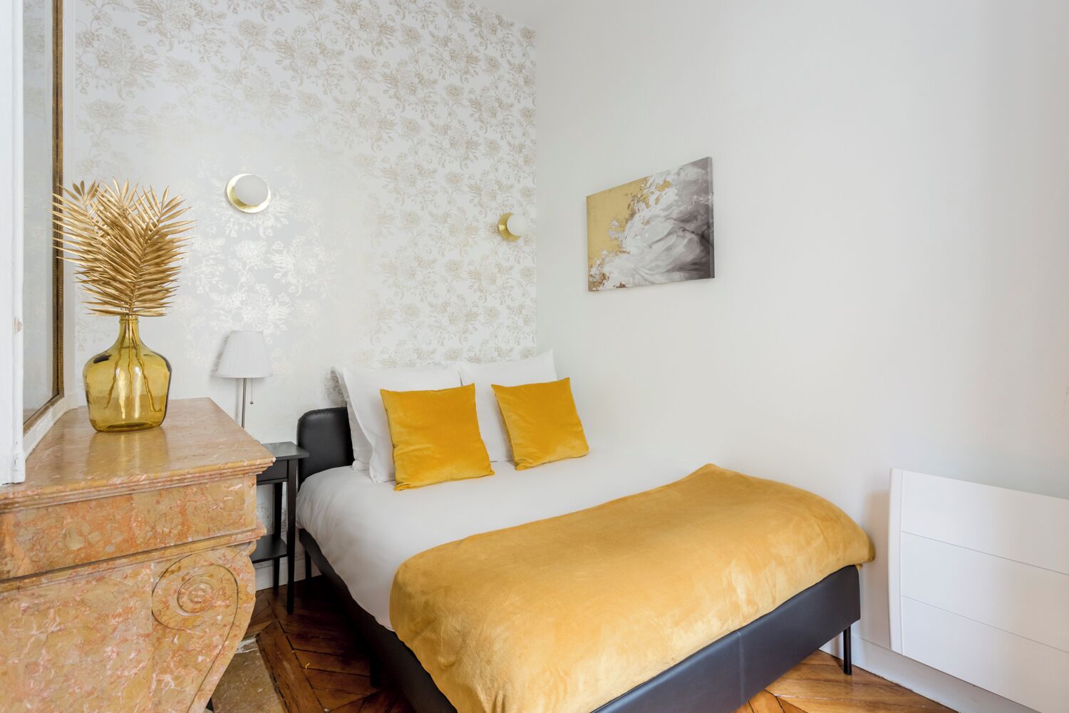 Ein Schlafzimmer mit einem Bett, einem Nachttisch, einer Lampe, einer Vase und einem Bild an der Wand.