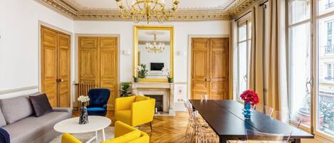 A room with a dining table, chairs, a sofa, and a chandelier.