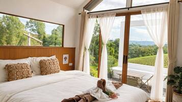 A spacious bedroom with a large bed, a view of greenery, and a balcony with a table and chairs.