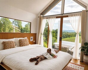 A spacious bedroom with a large bed, a view of greenery, and a balcony with a table and chairs. - Nai Suan Phan Resort - ในสวนฝัน รีสอร์ท (Khao Kho)