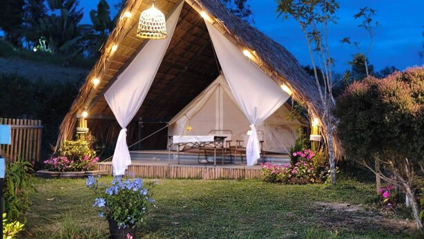 A thatched-roof tent with a dining area and a hanging light fixture.