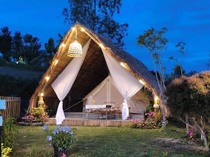 Een tent met rieten dak, een eethoek en een hanglamp.