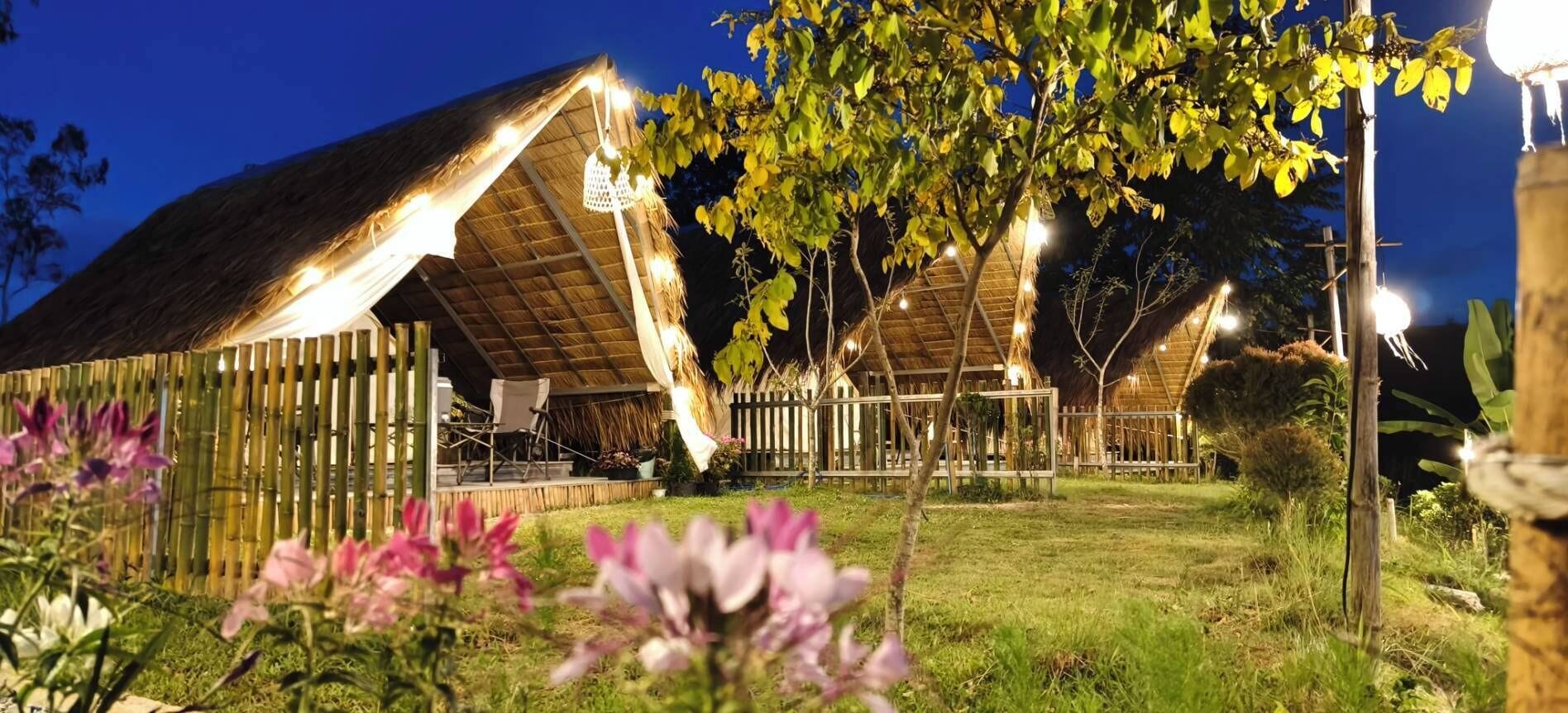 A thatched-roof building with a covered outdoor seating area, surrounded by greenery and flowering plants.