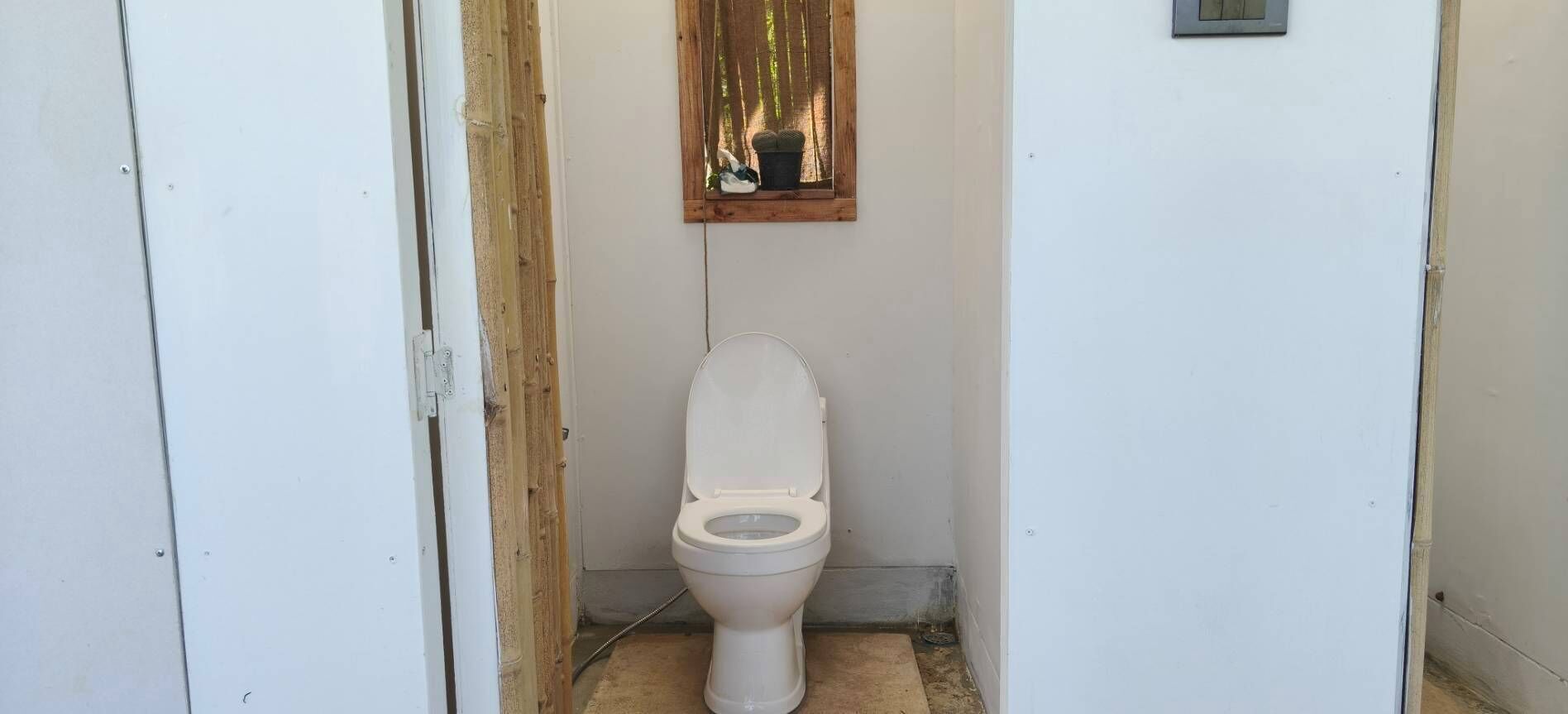Une petite salle de bain étroite, avec des toilettes, une fenêtre à cadre en bois et un petit luminaire fixé au mur.