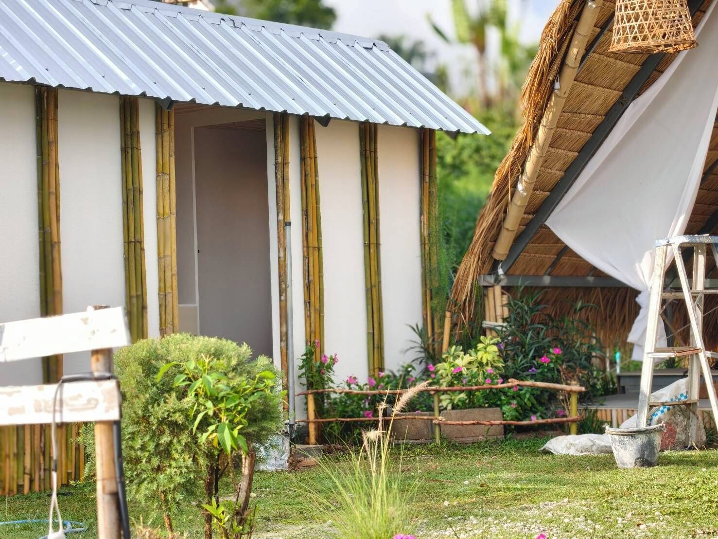 A house with a corrugated metal roof, bamboo pillars, and a thatched roof extension.