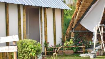 A house with a corrugated metal roof, bamboo pillars, and a thatched roof extension.
