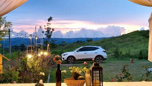 A white SUV parked on a grassy hill with a sunset view, string lights, and a lantern on a table.