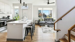 Una cocina moderna con una isla central, taburetes de bar y una zona de comedor con sofá y mesa de centro.