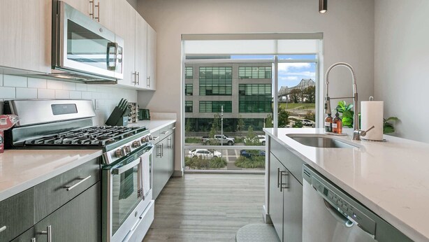 A modern kitchen with stainless steel appliances, a large window, and a view of a parking lot. - Riverscape Townhome (Baton Rouge)