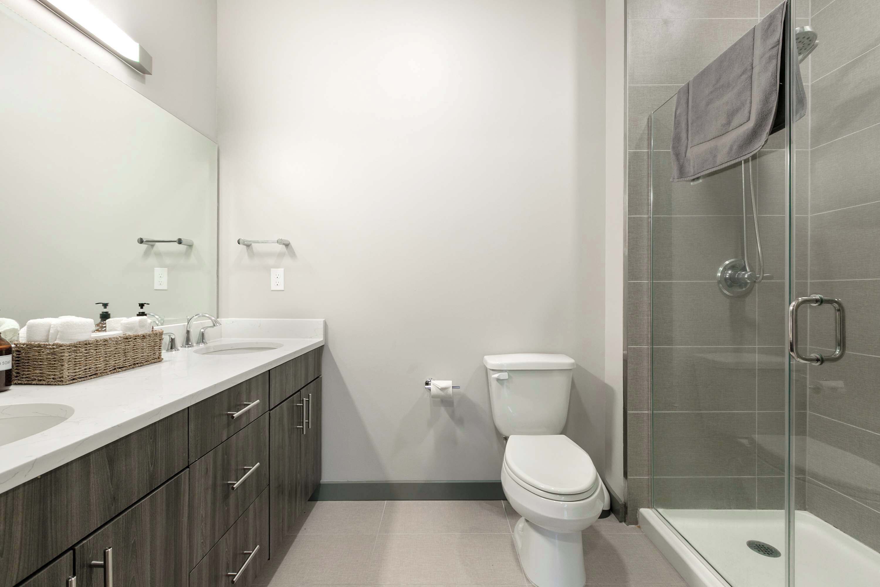 A modern bathroom with a glass shower enclosure, a white toilet, and a vanity with a mirror and two sinks.