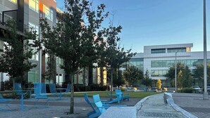 A modern outdoor seating area with blue chairs and tables, surrounded by trees and buildings. - Riverscape Townhome (Baton Rouge)