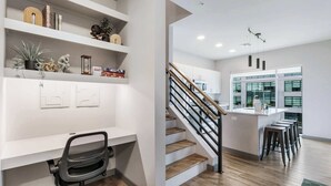A modern kitchen with a central island, wooden flooring, and a staircase leading to an upper level. - Peaceful Modern Townhome | Water Campus (Baton Rouge)