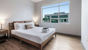 A modern bedroom with a large window, a wooden bed, and a nightstand with a lamp. - Peaceful Modern Townhome | Water Campus (Baton Rouge)