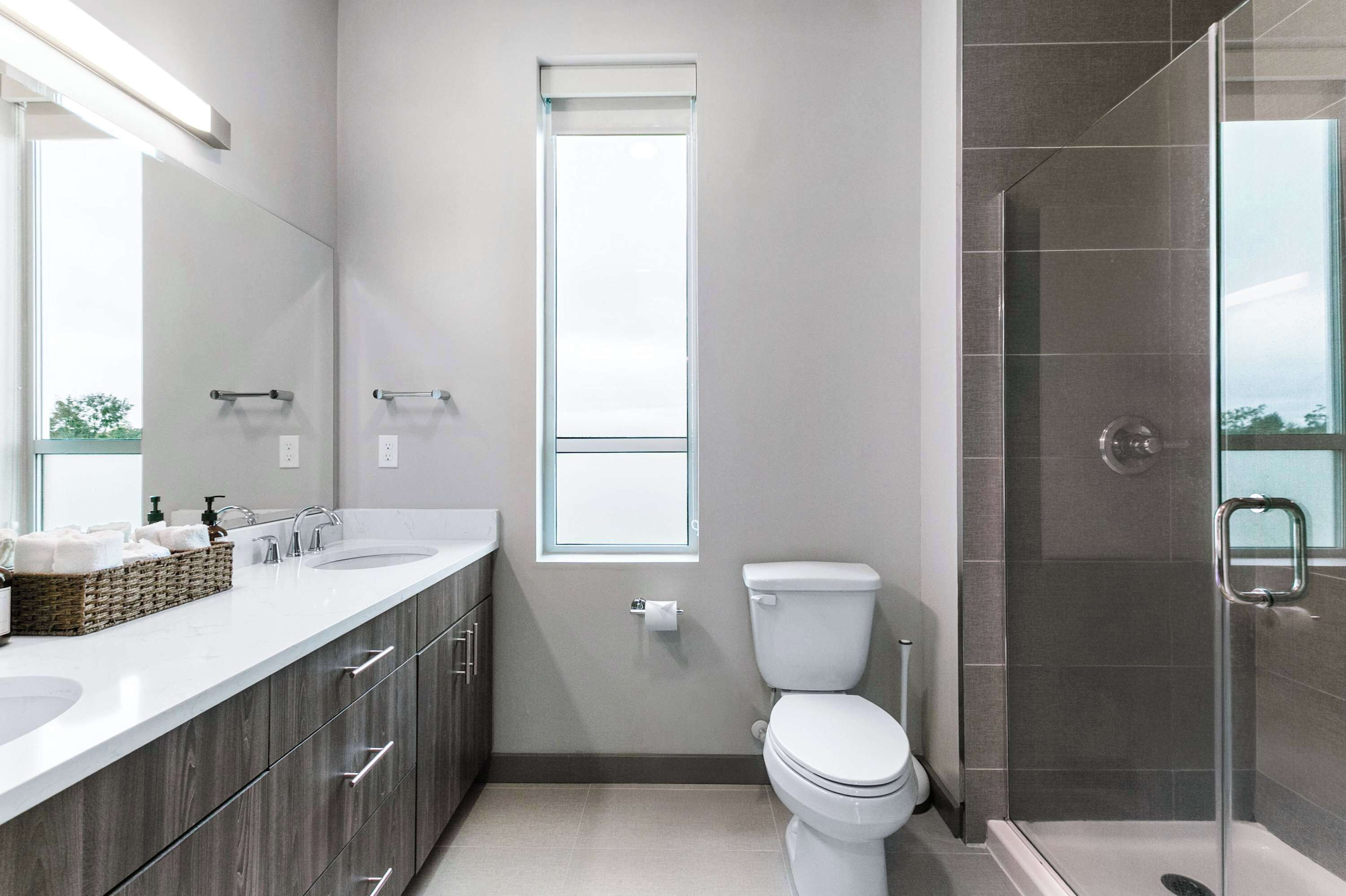 Een moderne badkamer met een wastafelmeubel met dubbele wastafel, een toilet en een douche met glazen wanden.