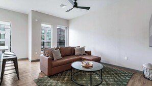 A modern living room with a brown leather sofa, a glass coffee table, and a ceiling fan. - Peaceful Modern Townhome | Water Campus (Baton Rouge)