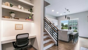 A modern kitchen with wooden flooring, a built-in island with bar stools, and a staircase leading to a dining area.