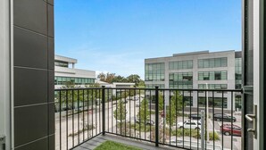 A balcony with a view of a modern building and a parking area.