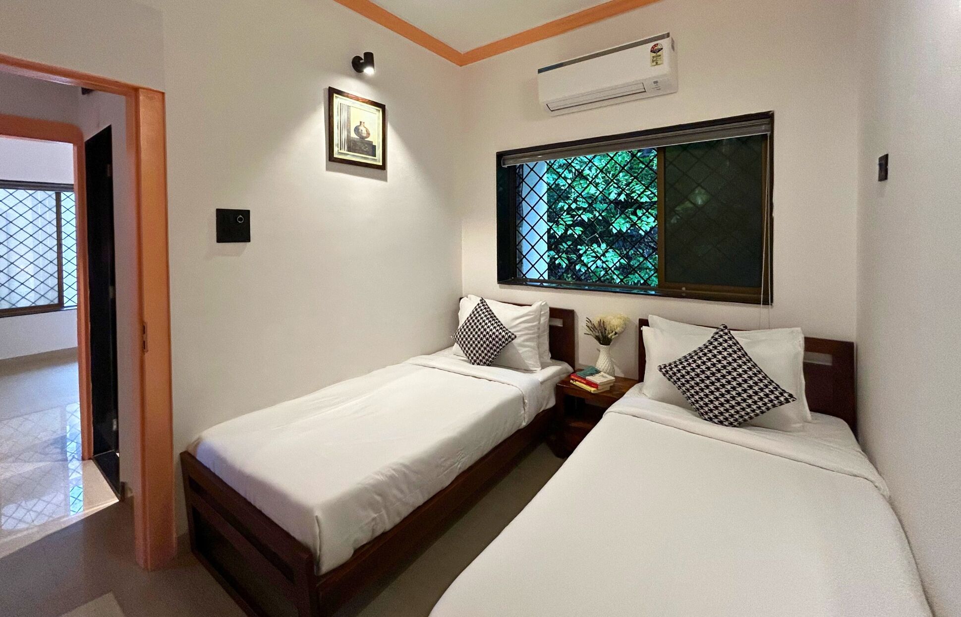 Habitación de hotel con dos camas individuales, una ventana con vistas a zonas verdes, un equipo de aire acondicionado y un cuadro en la pared.