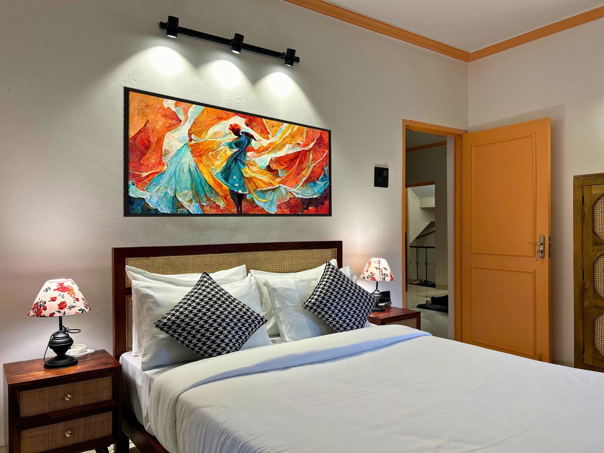 A hotel room with a large bed, two nightstands with lamps, a wooden door, and a colorful abstract painting on the wall.