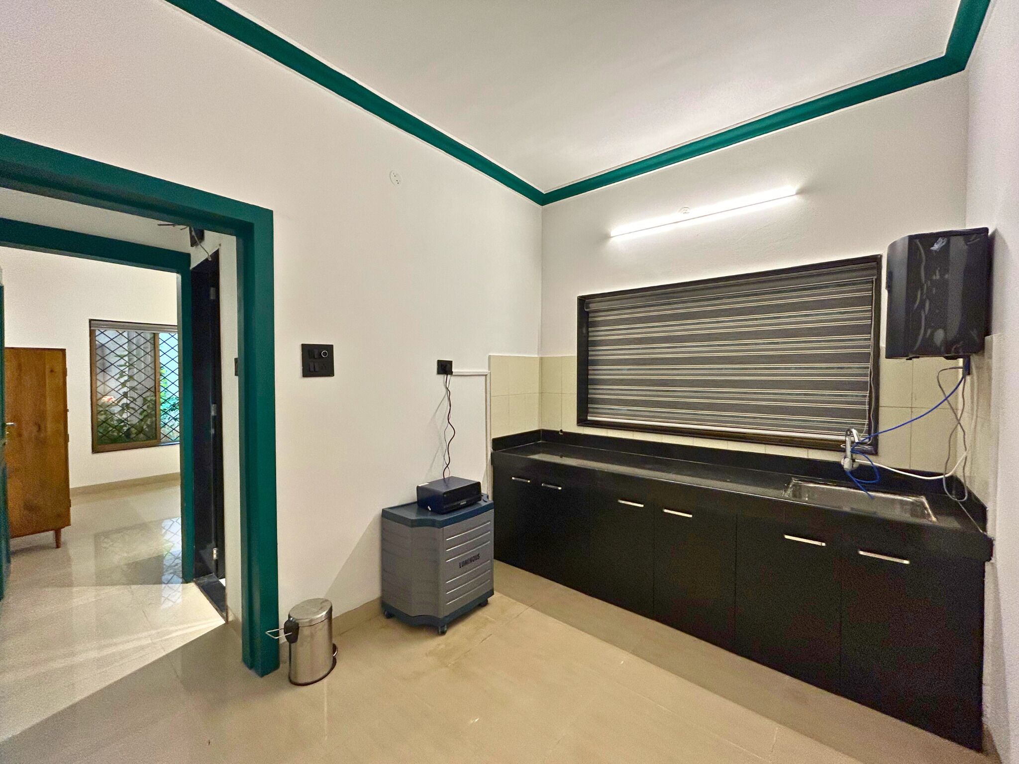 A kitchen with black cabinets, a stainless steel sink, and a window with horizontal blinds.