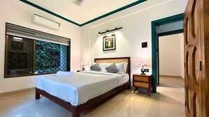 Une chambre à coucher bien aménagée, avec un grand lit, des tables de chevet avec des lampes, un ventilateur de plafond et une fenêtre donnant sur des arbres.