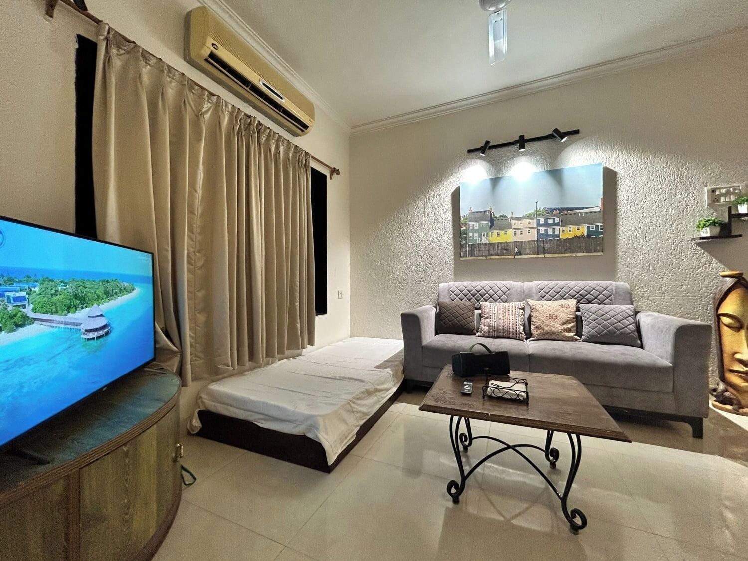 A living room with a sofa, a coffee table, a TV, and an air conditioning unit.