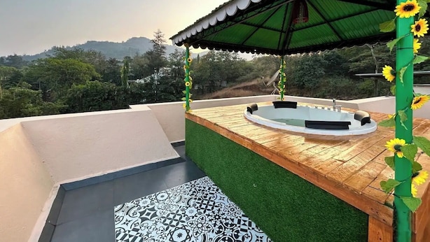 Un espace piscine aménagé sur le toit, avec une terrasse en bois, de l’herbe artificielle verte et une bordure décorée de carreaux à motifs.