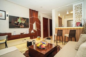 A modern living room with a wooden coffee table, a sofa, and a dining area with bar stools. - Domaine d'Anfa | Luxurious Appt | Pool & Sea (Casablanca)