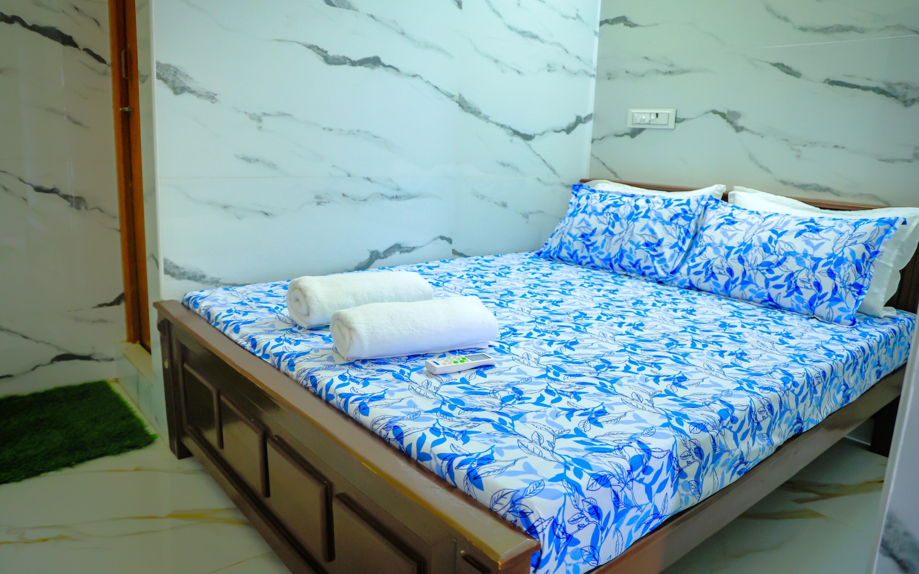 A bed with a blue floral bedspread, two white towels, and a remote control on the bed.