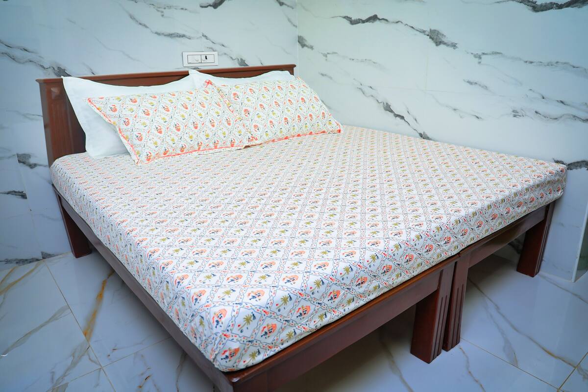 A bed with a patterned bedspread and pillows, a wooden headboard, and a marble-patterned wall.