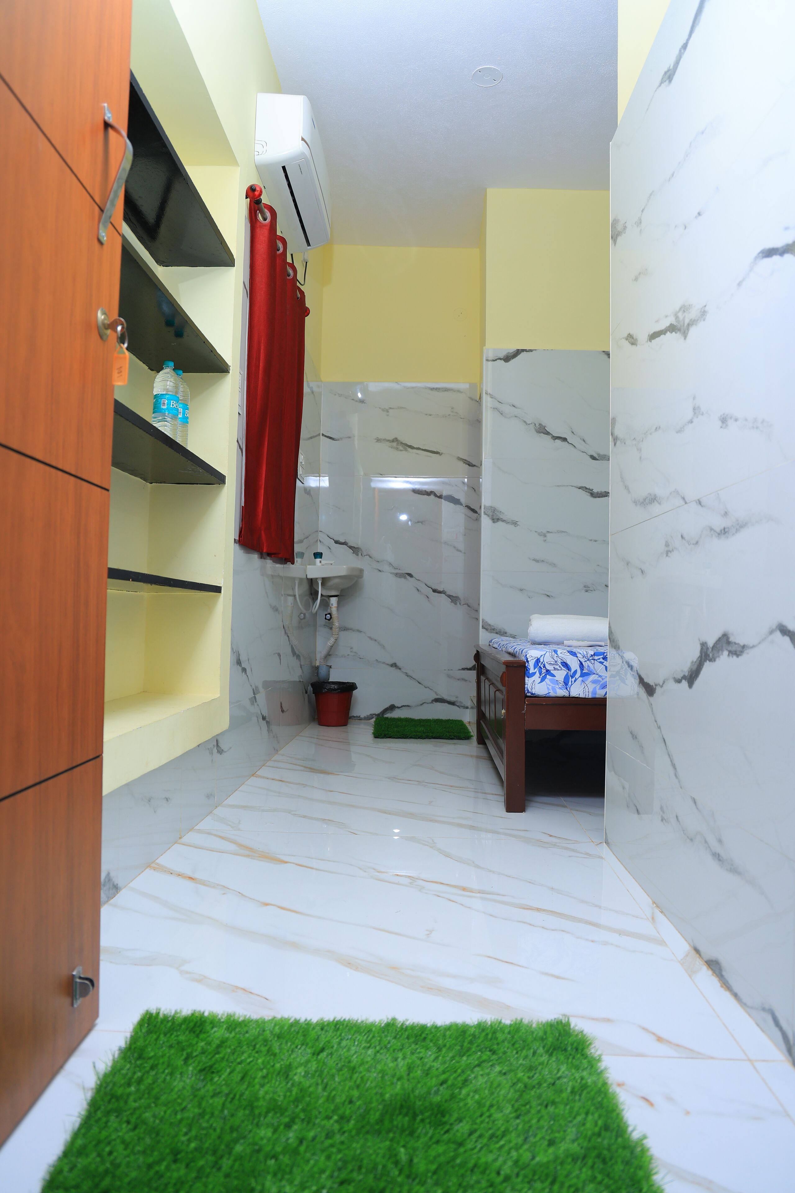 A bathroom with a marble wall, a wooden cabinet, a red curtain, a sink, a green mat, and a small wooden stool.