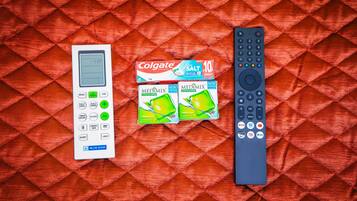Et hvidt digitalt ur, en Colgate tandpastaæske og en fjernbetjening på en rød, quiltet overflade.