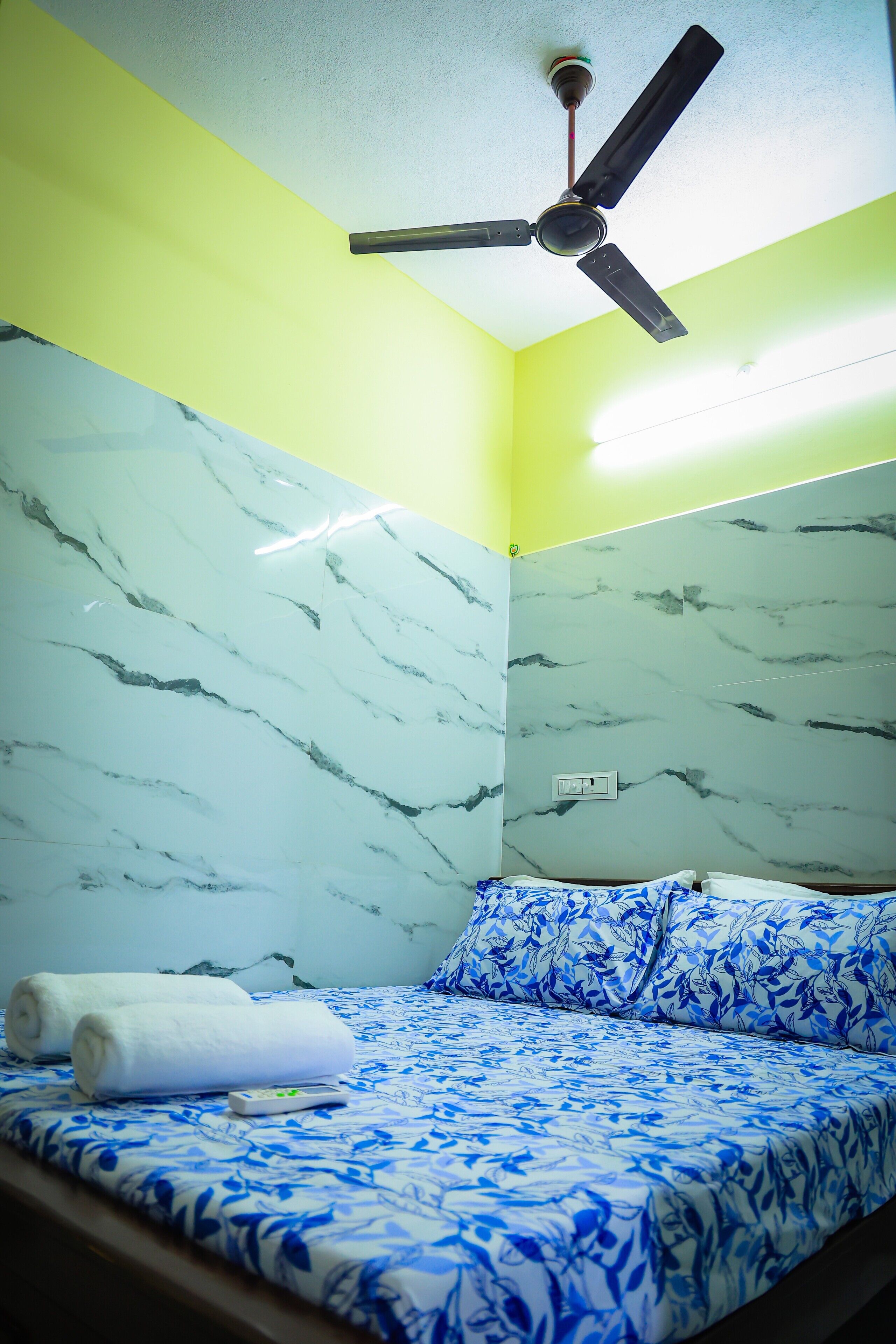Um quarto com cama, ventoinha no teto e paredes com padrão marmorizado.
