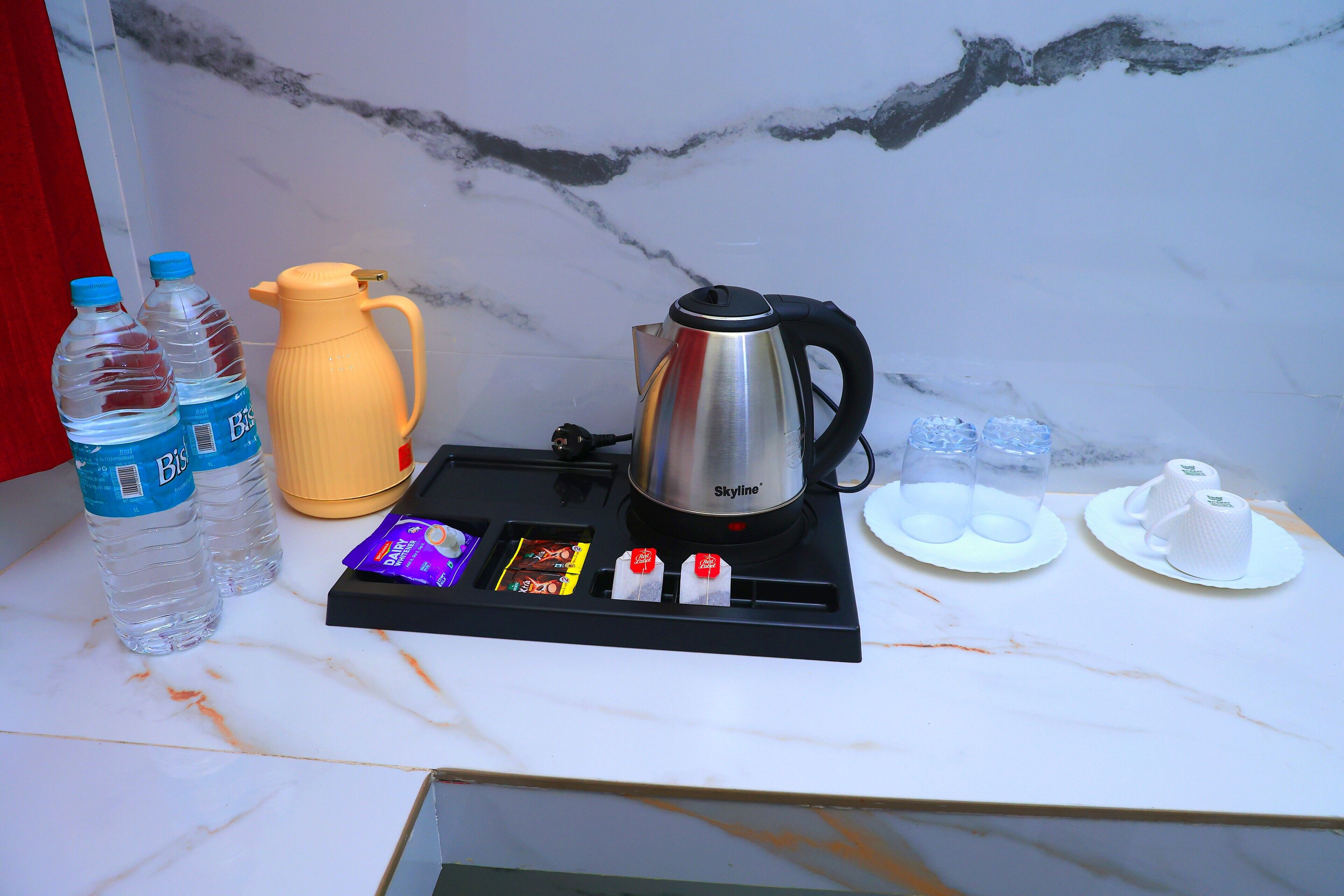 Una encimera de cocina con una cafetera, botellas de agua, sobres de té y un hervidor.