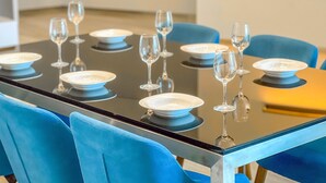 Mesa de comedor dispuesta con platos y copas de vino, rodeada de sillas azules.