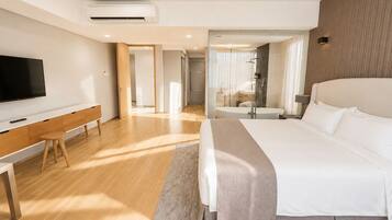 A modern hotel room with a large bed, a desk, a flat-screen TV, and a bathroom with a bathtub and shower.