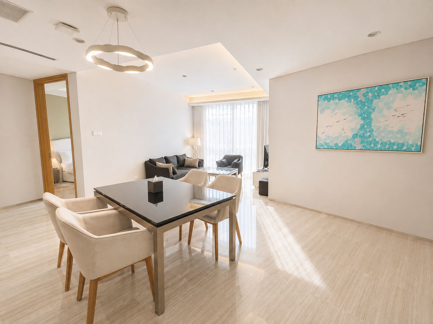 A modern hotel room with a dining area, a sofa set, and a large abstract painting.