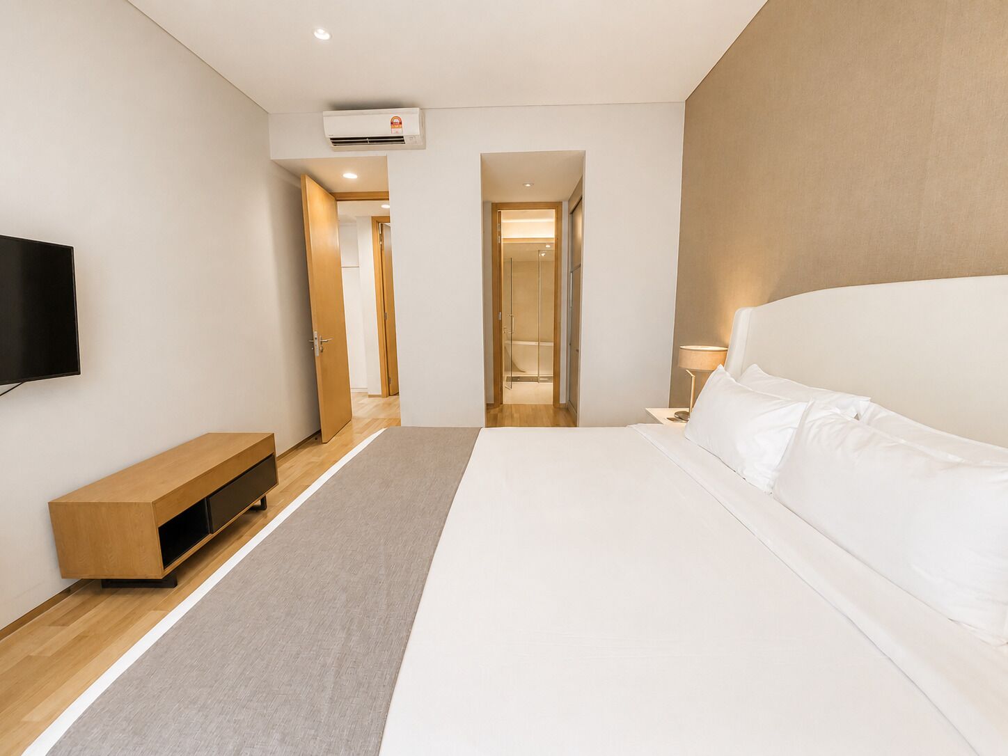 A modern hotel room with a large bed, a flat-screen TV, a wooden bench, and a walk-in shower.