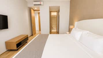 A modern hotel room with a large bed, a flat-screen TV, a wooden bench, and a walk-in shower.