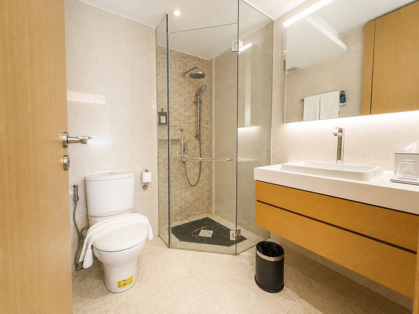 Une salle de bain moderne avec une douche à parois de verre, des toilettes, un lavabo et une poubelle.