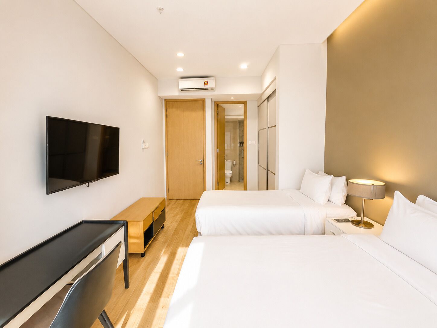 Una habitación de hotel con cama, mesita de noche, lámpara, televisor y un pequeño escritorio.