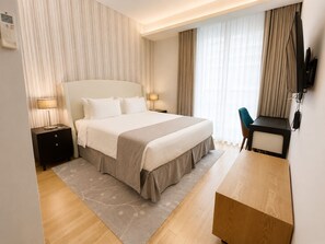 Una habitación de hotel con una cama grande, mesitas de noche, un escritorio y un televisor.