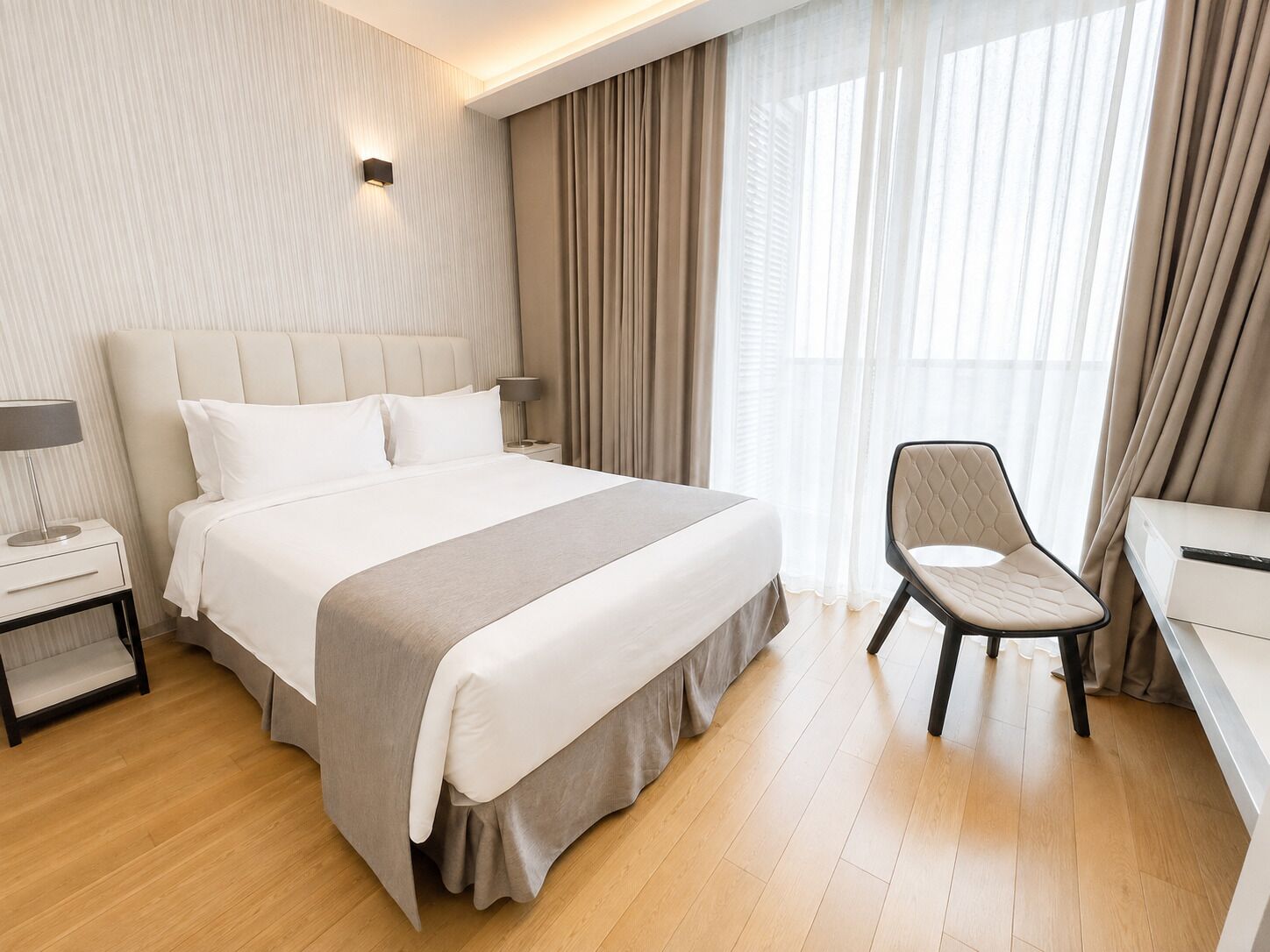 A hotel room with a large bed, a chair, a desk, and a nightstand.