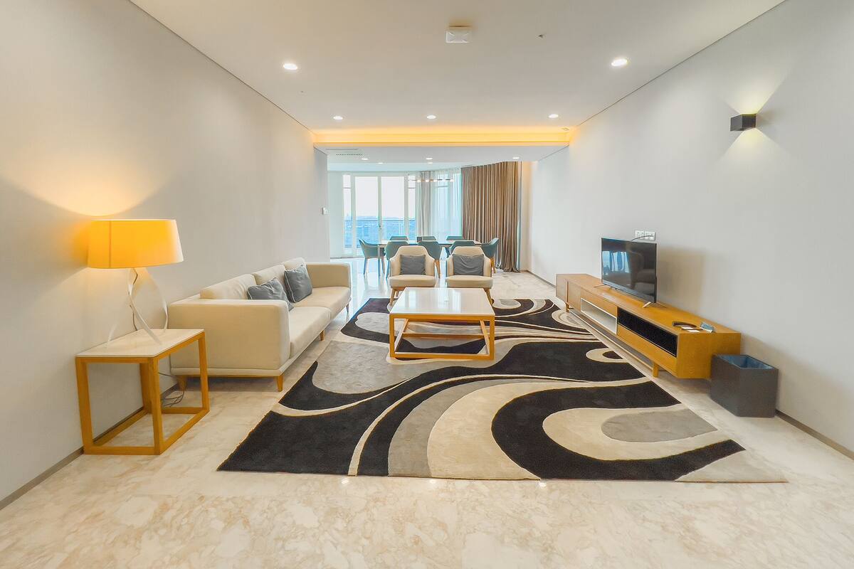 A modern living room with a sofa, coffee table, TV, and a view of the city through large windows.