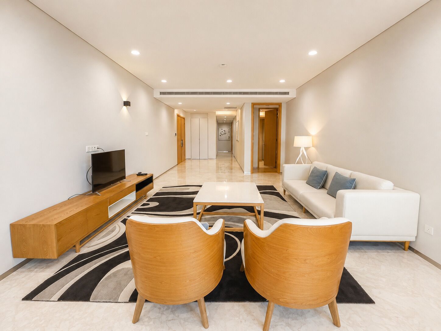A modern living room with a flat-screen TV, wooden furniture, a sofa, and a lamp.
