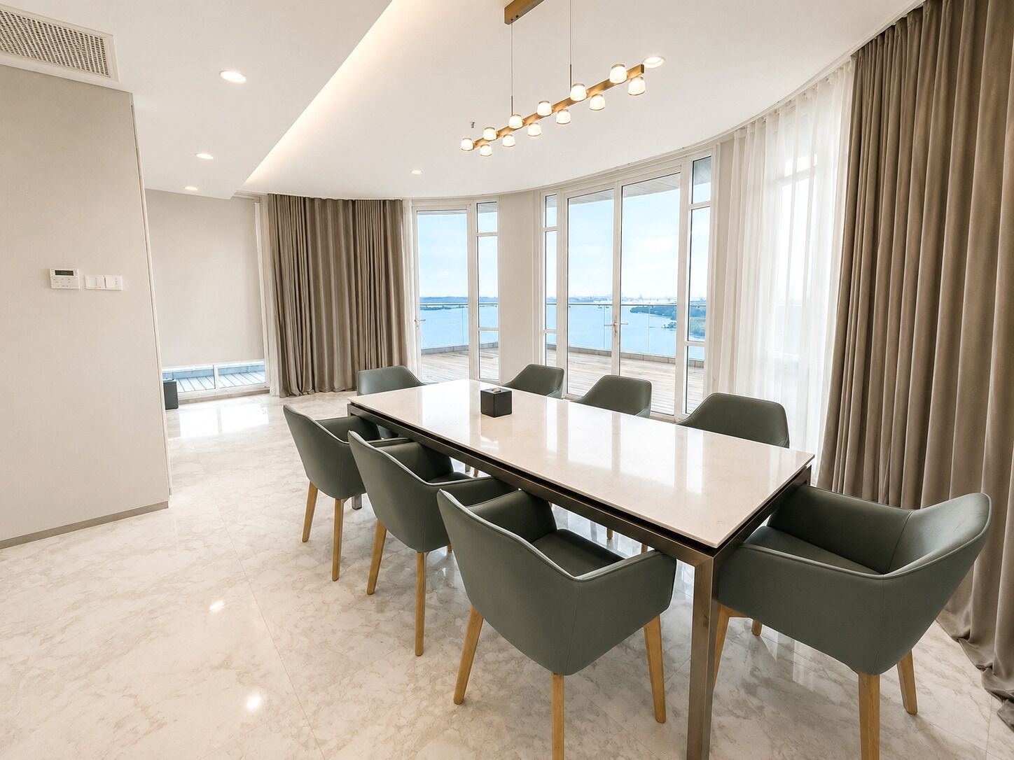 Une salle de conférence dotée d’une grande table, de six chaises, d’un lustre moderne et offrant une vue sur la mer grâce à de larges fenêtres.