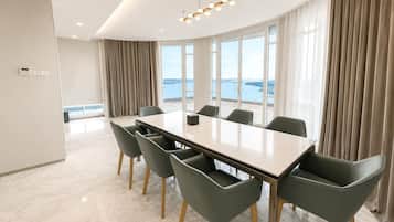 Un salón de conferencias con una mesa grande, seis sillas, una lámpara de araña moderna y vistas al mar a través de amplias ventanas.