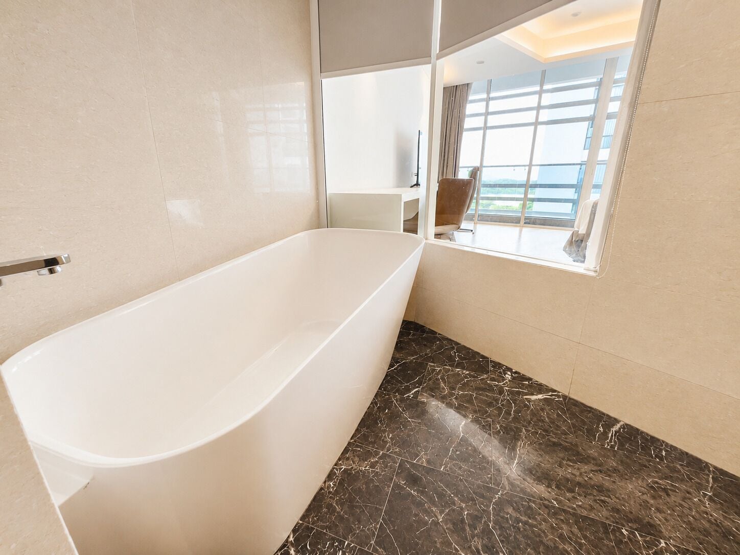 Un baño moderno con una bañera independiente, un amplio ventanal con vistas y suelo de mármol.