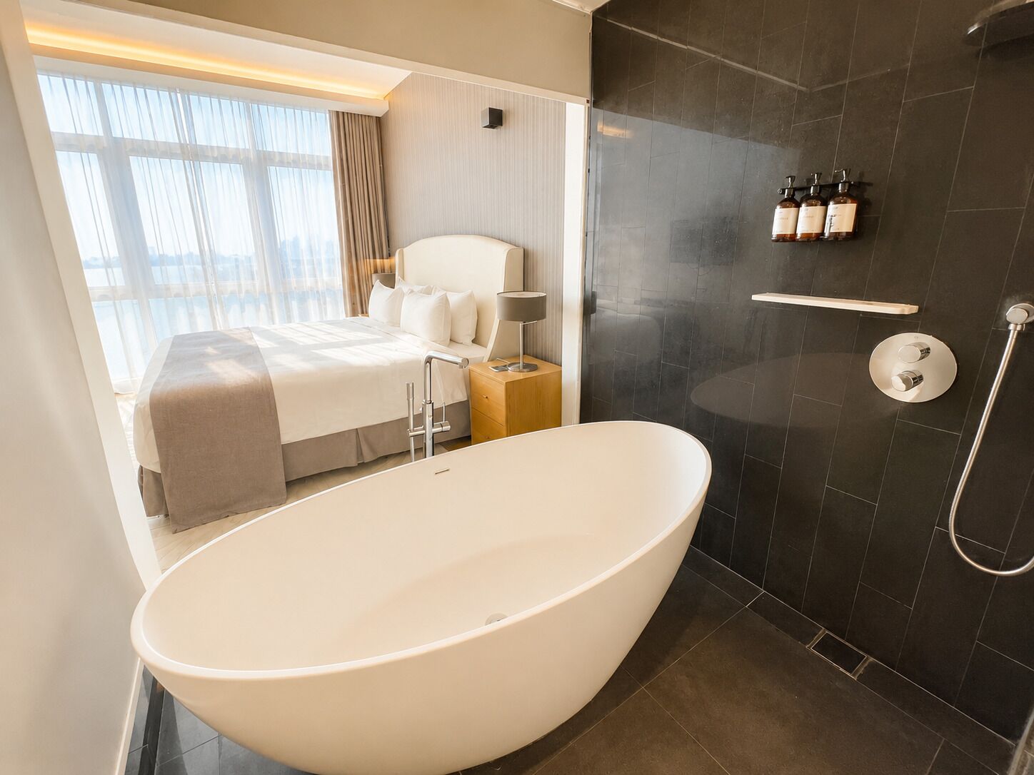 A modern bathroom with a freestanding bathtub, a shower area, and a bedside table with toiletries.